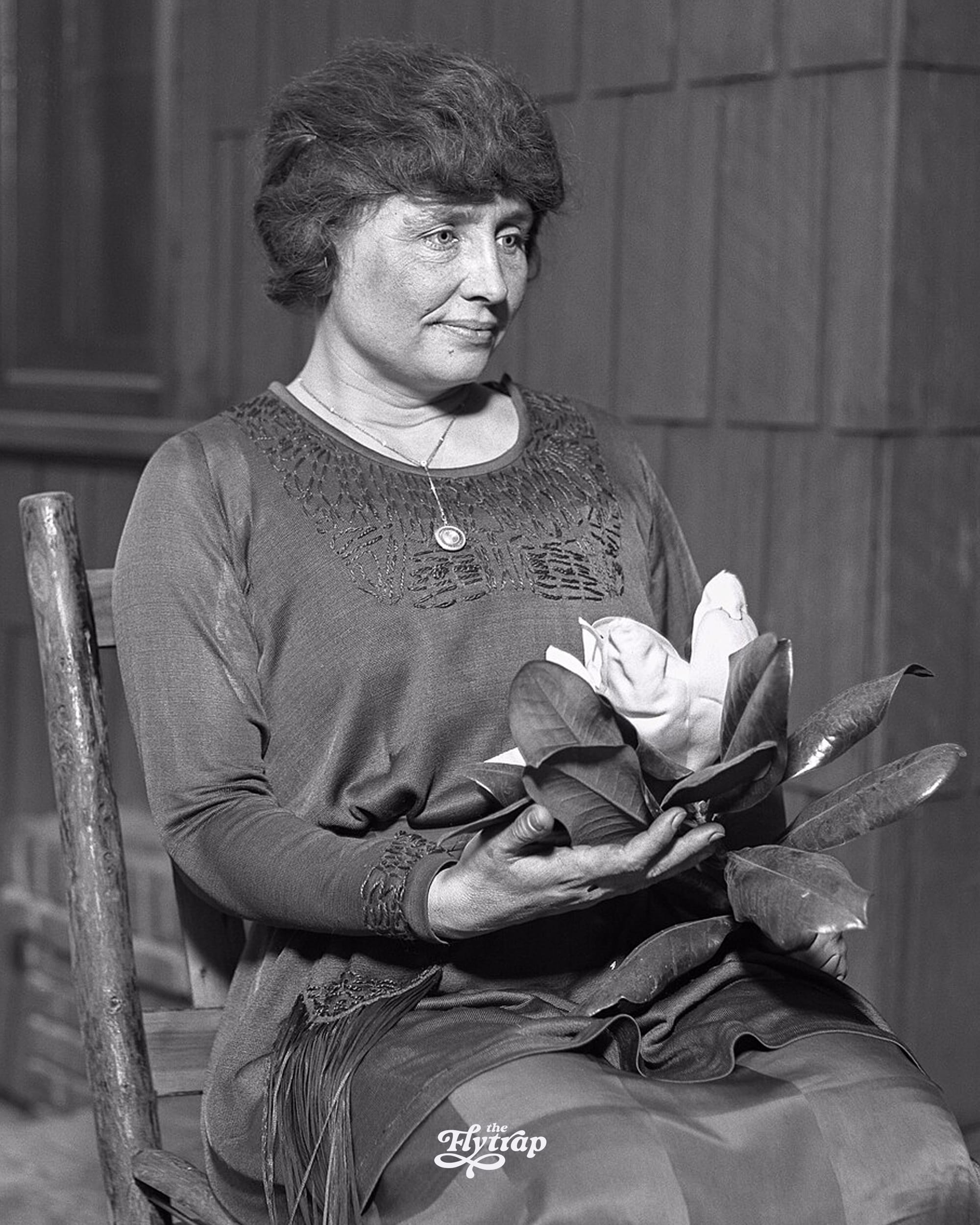A black and white photograph of Helen Keller holding a magnolia bloom