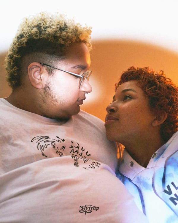 A fat brown-skinned and a smaller brown-skinned person, both with short curly hair, looking lovingly at each other.